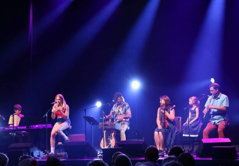 Six people sit on a stage playing instruments.