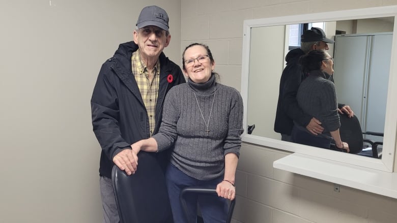 Lawrence Shebib and Debbie Murphy stand behind a salon chair, facing the camera, at the newly created hair salon at the North Sydney Food Bank.