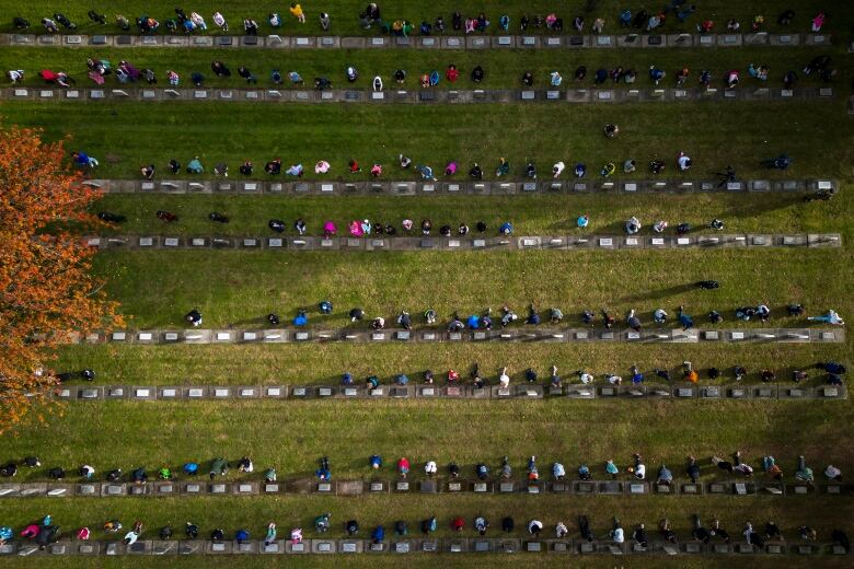 A drone image taken from above shows people kneeling at gravestones.