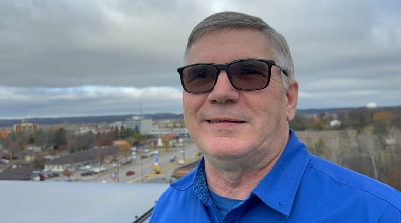 A man in sunglasses and a blue shirt stands on a roof top 