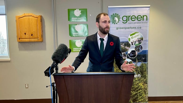 Man in suit stands at podium with blue and green poster behind him.