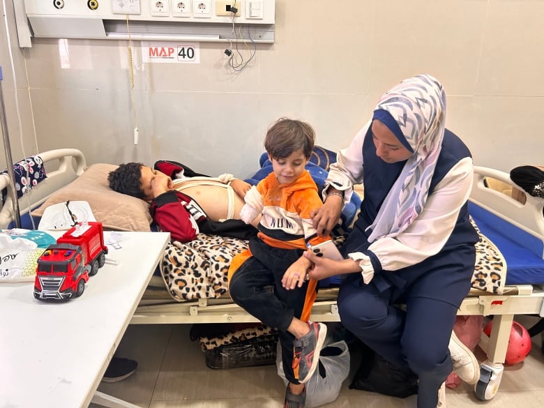 A woman sits on a hospital bed next to two young boys.