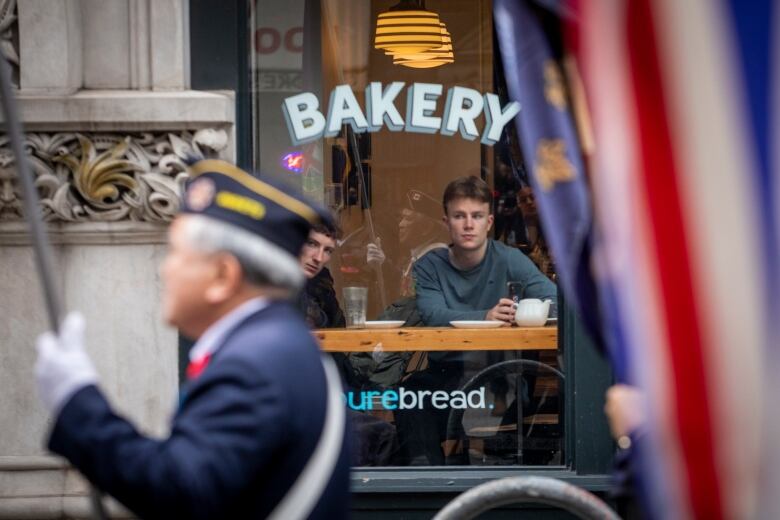 A man in a bakery watches as veterans march down East Hastings Street.