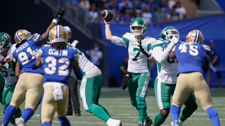 A quarterback in green and white throws the football while linemen from both teams battle.