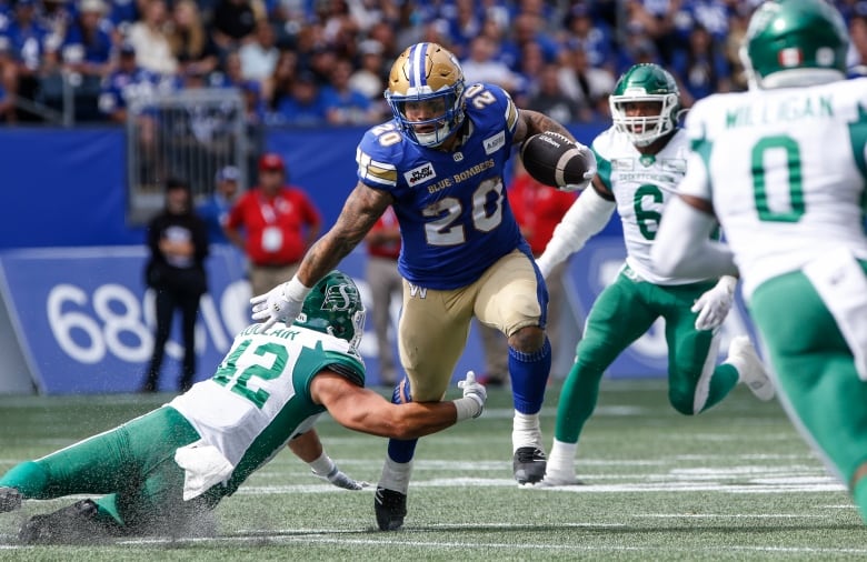 A ball-carrier in blue and gold runs through an attempted tackle below his knees by a player in green and white.