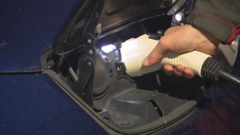 A person's hand plugging in an EV charger to a blue car.