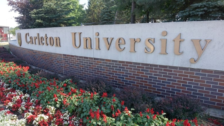 The sign for Carleton University is pictured with flowers in front. 