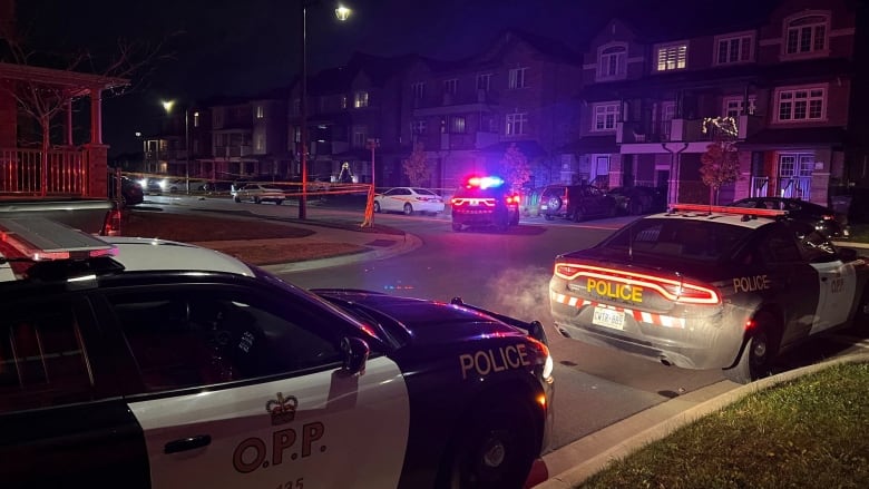 Three police cars are parked on a street outside an apartment building at night. 