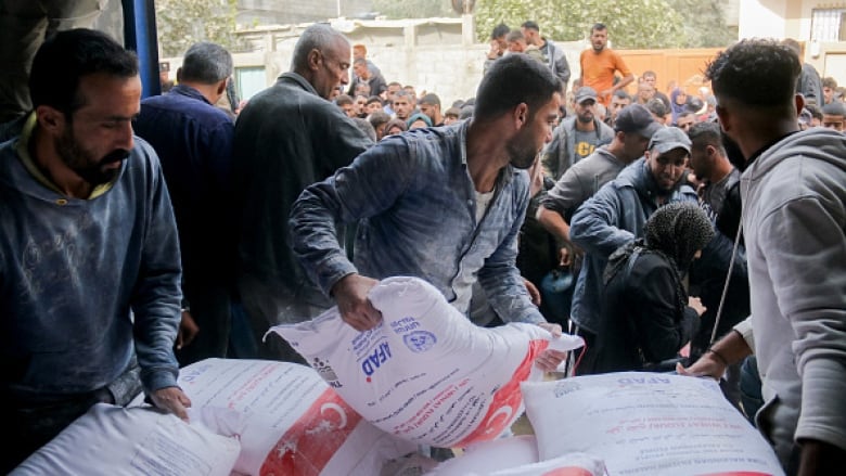 Men lift bags of food off a truck. A crowd of people surge behind them.