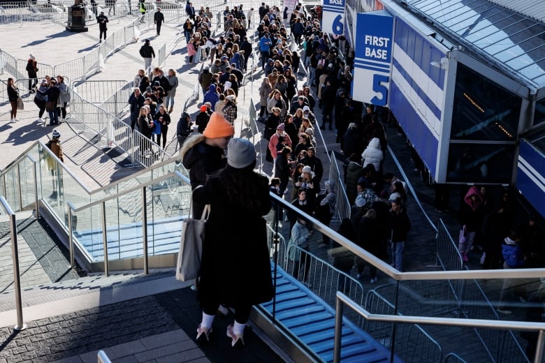 Two people atop a set of stairs looking down on a lineup of Taylor Swift fans outside Rogers Centre.