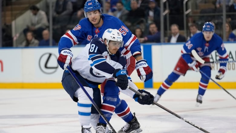 A hockey player in a blue jerseys commits a foul against the player in a white jersey.