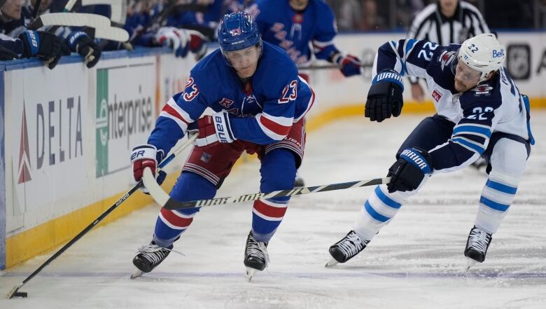 Two players fight for a loose puck along the boards.