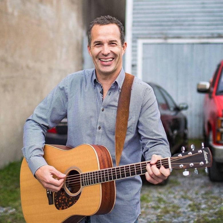 Man smiling and holding a guitar.