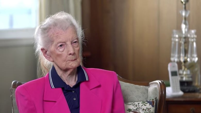 An elderly woman with white hair in a pink suit. 