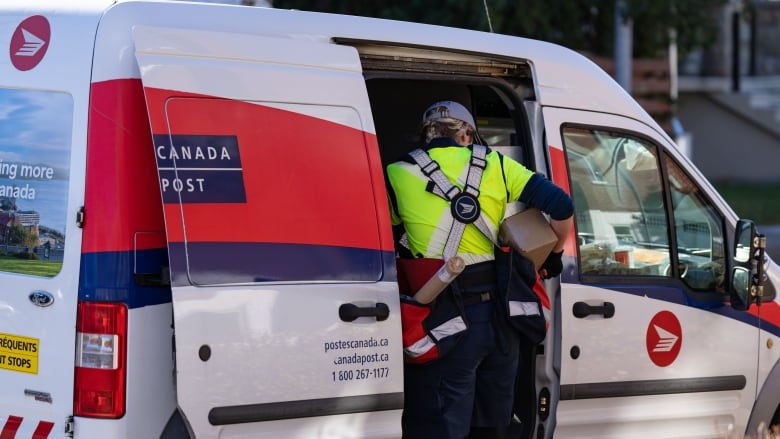 A mail carrier gets mail out of their work vehicle.