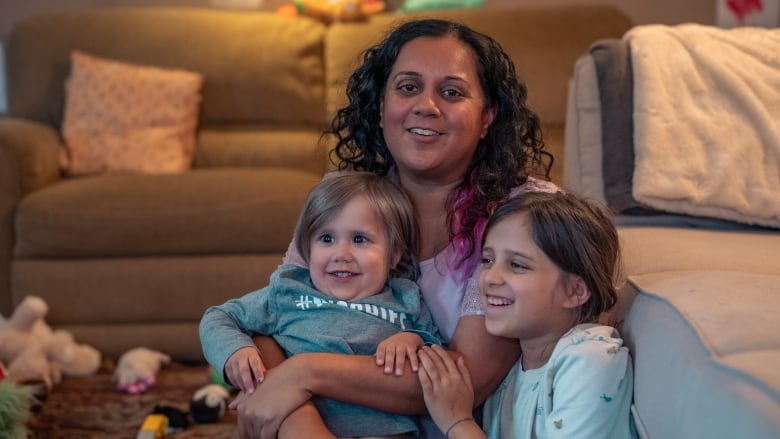 A mom holds her two children  4-year-old Manny and 9-year-old Jasmine  in her arms. All three are sitting on the living room floor, smiling.