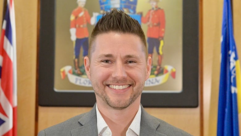 A man in a grey blazer smiles in a close-up photo.