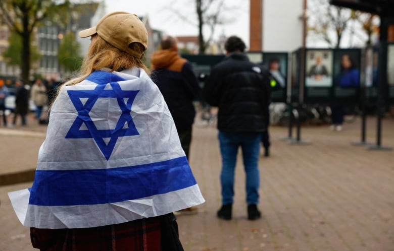 A woman wrapped in an Israel flag stands outside the place where mayor of Amsterdam Femke Halsema attends a press conference following the violence targeting fans of an Israeli soccer team, in Amsterdam, Netherlands, November 8, 2024. 