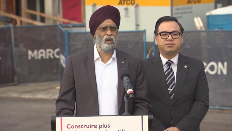 A man stands at a podium in front of a construction project. 