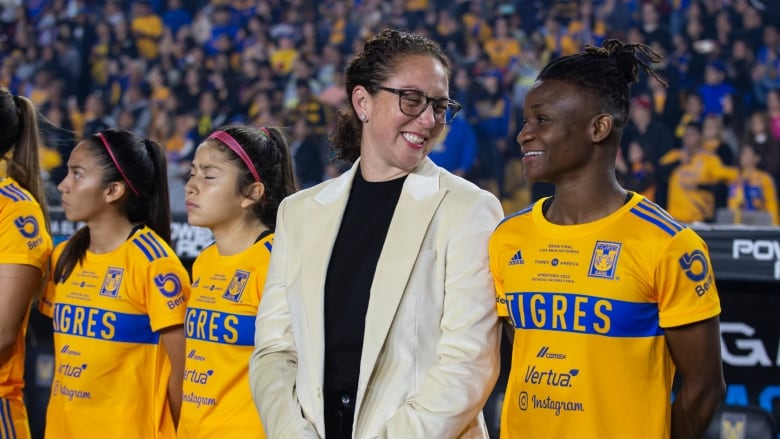 A woman's soccer coach stands with her player on the sideline.