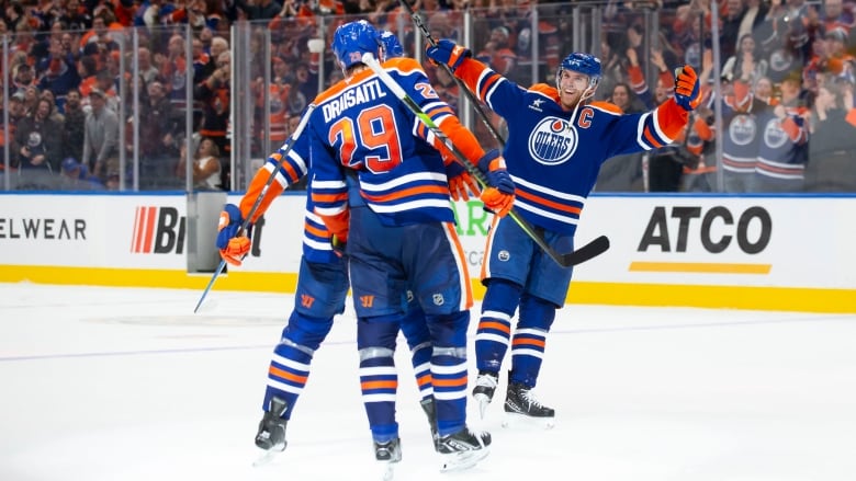 Three men's hockey players embrace in celebration on the ice during a hockey game.