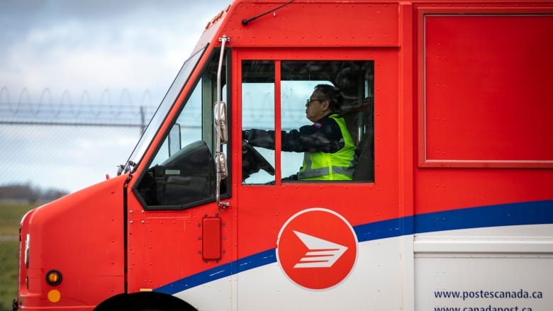 A postal worker is pictured in the driver's seat of a delivery truck.