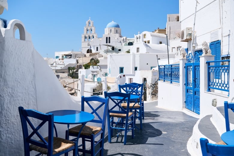 White concrete buildings with blue tables chairs in foreground.