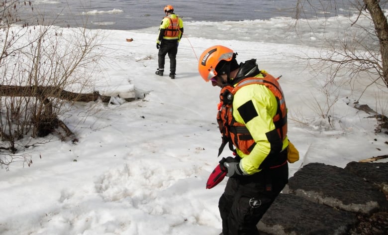 Police search a snowy landscape along a river.