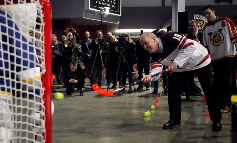 Premier John Horgan takes a shot on net against Celly the junior hockey mascot before Team Canada hopefuls practice during selection camp at the Q Centre in Victoria, B.C., on Tuesday, December 11, 2018. THE CANADIAN PRESS/Chad Hipolito