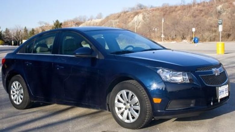 A blue 2011 Chevy Cruze LT Turbo in a parking lot near a hill of bare trees. 