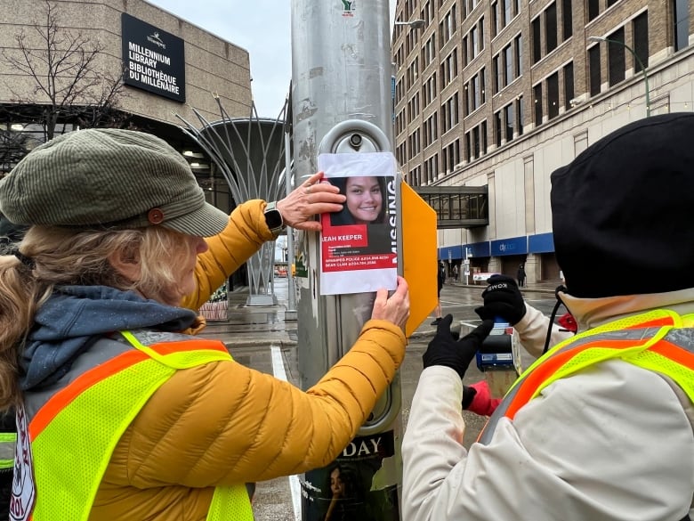 Two people paste a poster on a traffic light in Winnipeg's downtown