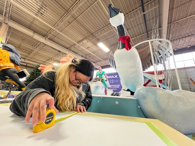 A woman uses measuring tape while working on a parade float. 