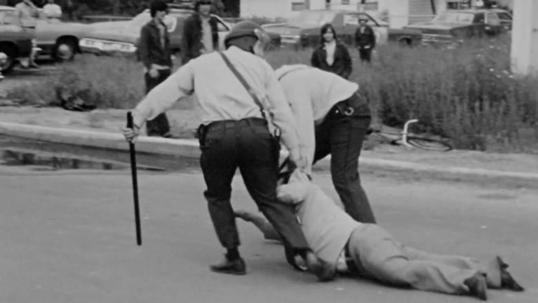 Two police officers dragging a person in a black and white photo.