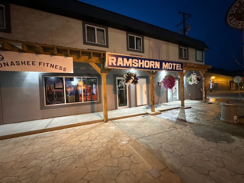 A photo of the outside of the Ramshorn Motel in Lumby B.C, at night. with a sign bearing the motel name in block letters and flower planters hanging from the front archway.