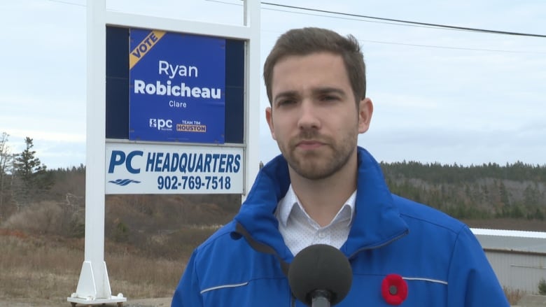 man wearing blue jacket stands outside next to sign