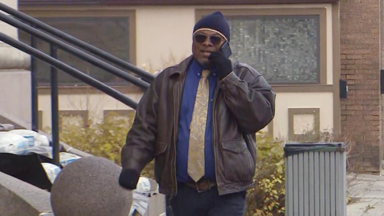 Man walks with sunglasses while speaking on a cell phone.