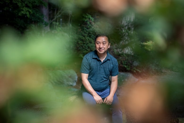 A man sits amid greenery, smiling.