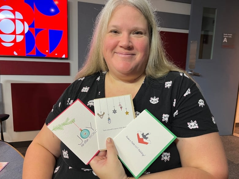 Woman with light hair and a black shirt holding up three cards.