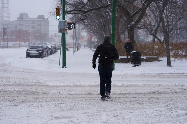 A person in black winter gear walks across a snowy street.