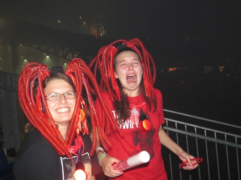 Two girls with red streamers on their head. The girl on the right is smiling big, while the girl on the left is sobbing.