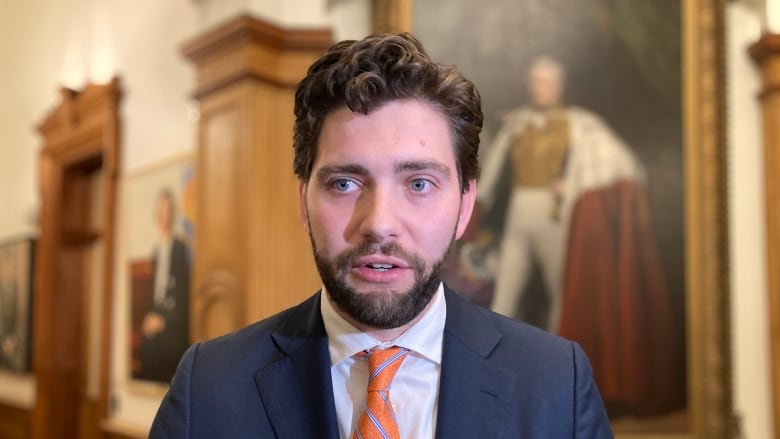 A man wearing a blue suit and orange striped tie with brown hair