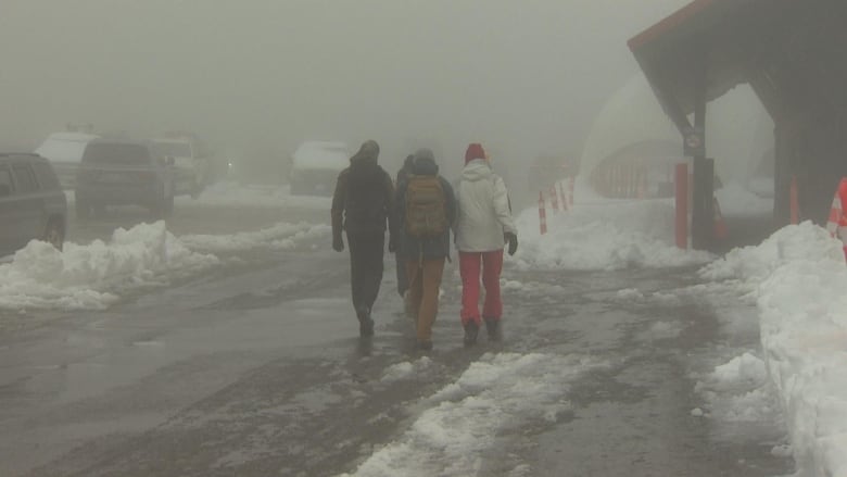 People walk past a snowy and slushy parking lot.