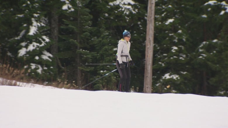 A woman skis past a range of trees.