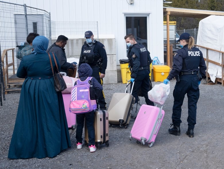 RCMP officers help a family of asylum seekers with their luggage as they cross the border at Roxham Road from New York into Canada on March 24, 2023 in Champlain, N.Y.