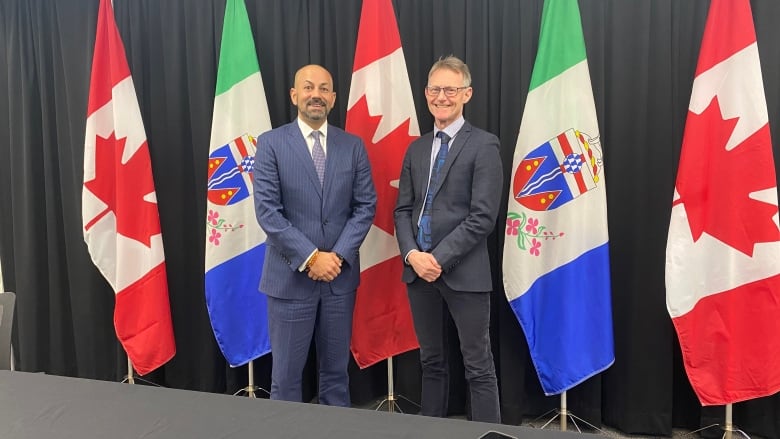 Two men in suits pose for a photo with Canadian and Yukon flags in the background.