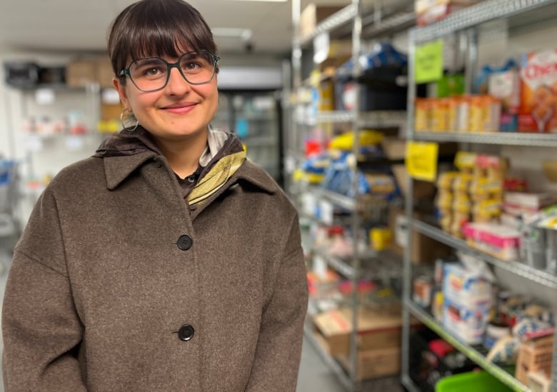 A young woman wearing glasses is shown inside a food bank.