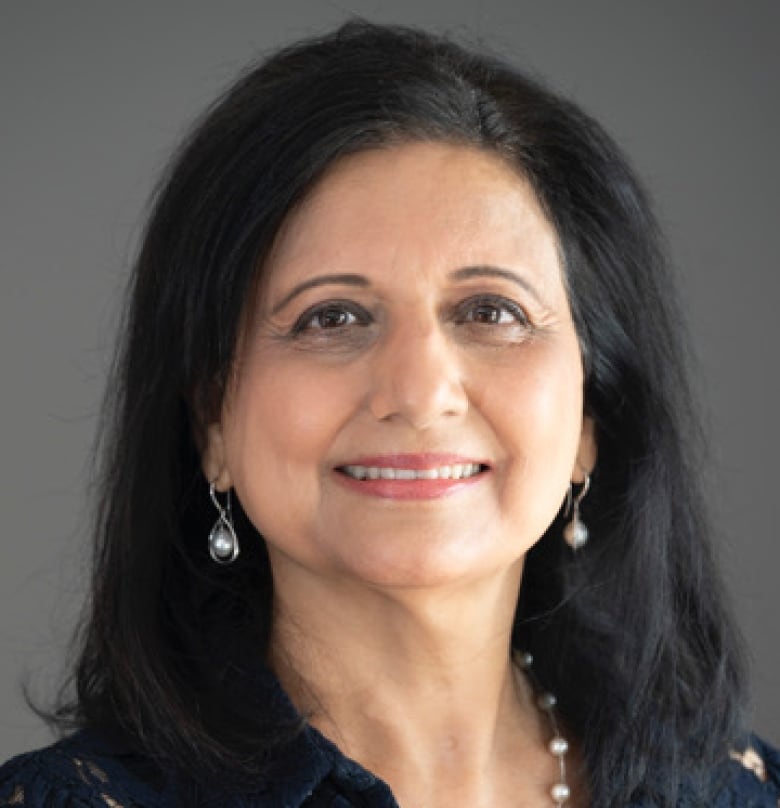 A woman with shoulder length black hair, smiling with red lipstick, white pearl drop earrings and a black blouse.