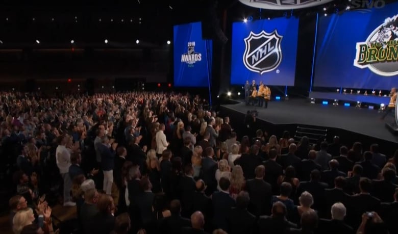 A large crowd looks toward a stage where several hockey players are standing. The NHL and Humboldt Broncos logos are in the background.