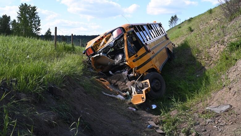 A yellow school bus with a destroyed bonnet lodged in a grassy ditch.