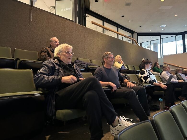 Two men, one with white hair sitting next to another man with short grey hair in council chambers in Sudbury.